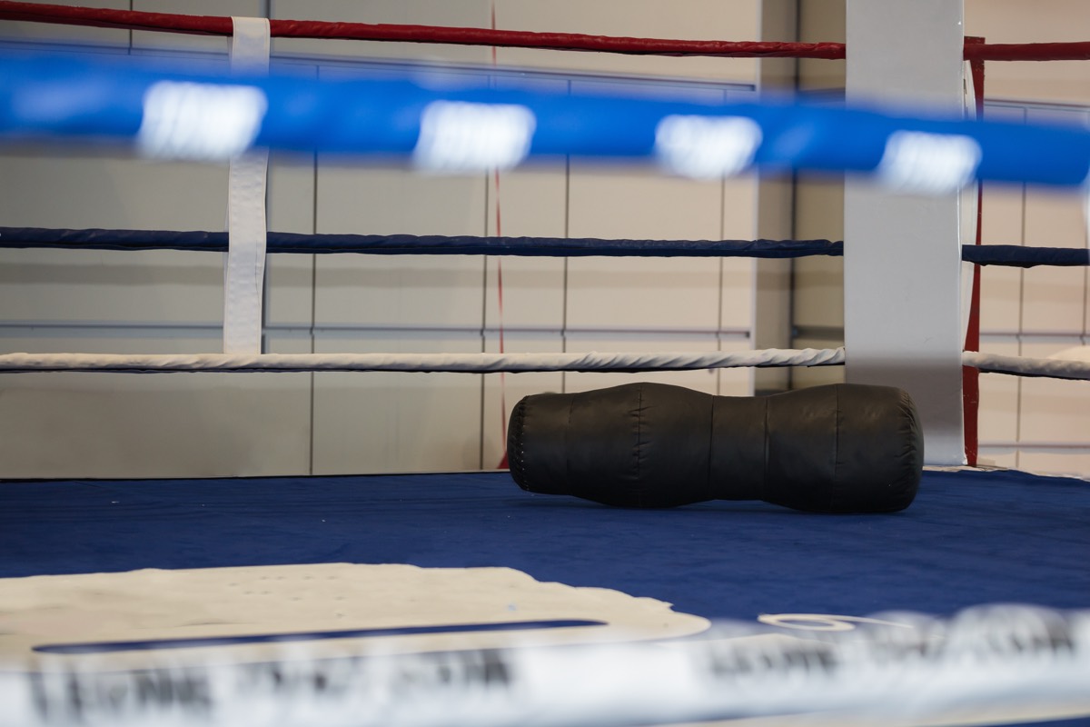 An empty boxing ring with ropes and corner stool under overhead lights