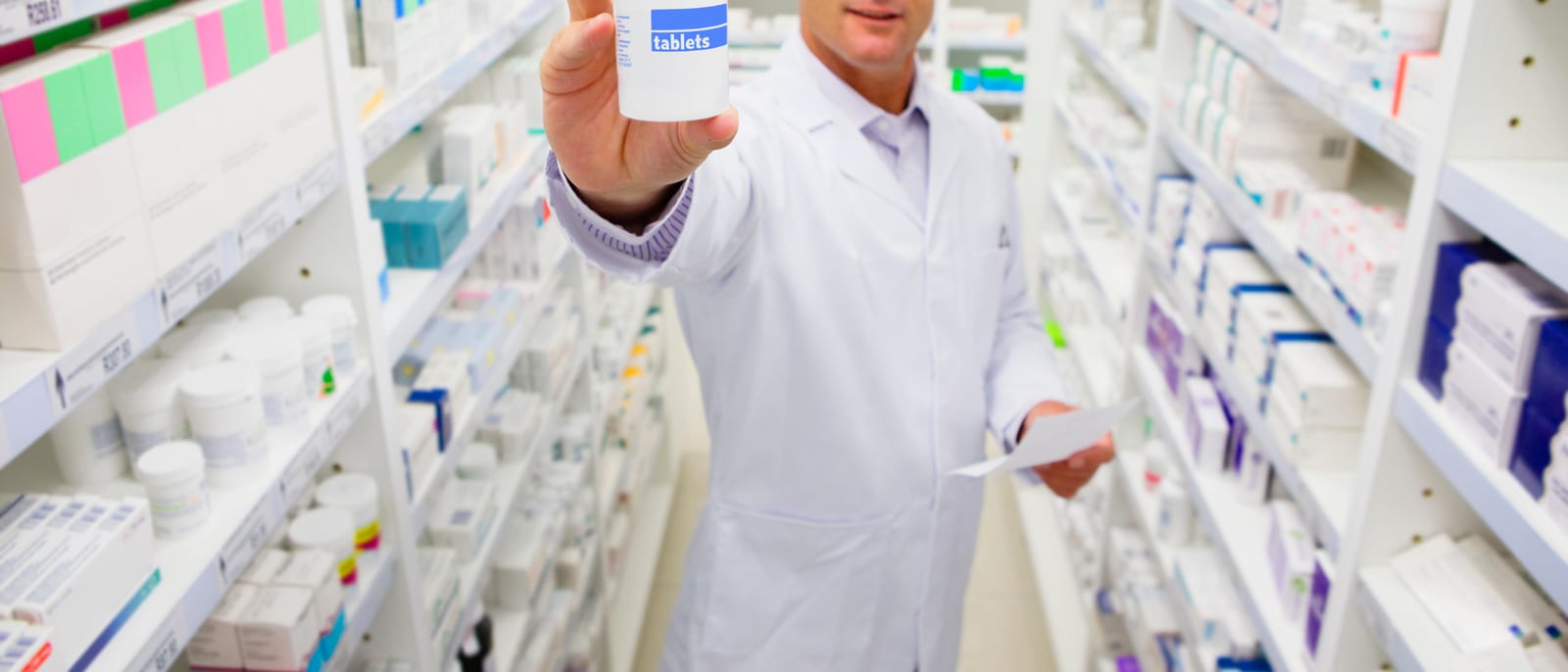 Rows of prescription pill bottles on a pharmacy shelf under bright light