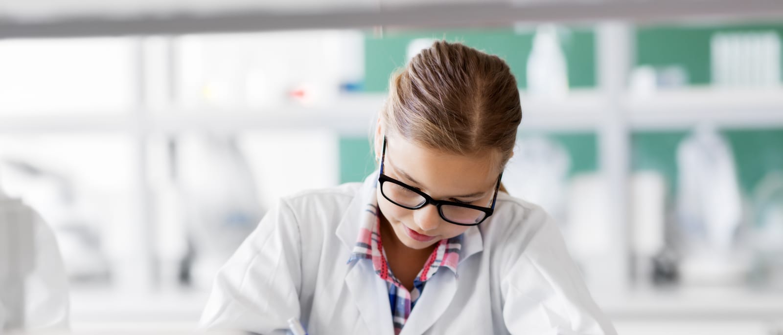 Researcher writing detailed notes beside laboratory glassware on a bench