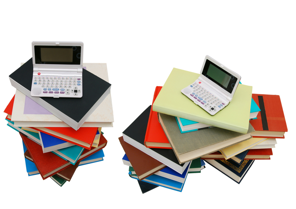 A person using a laptop beside a stack of library books with a magnifying glass