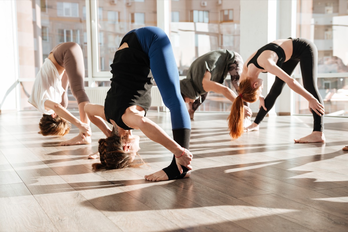 A group yoga class holding a standing posture on mats in a warm, softly lit studio
