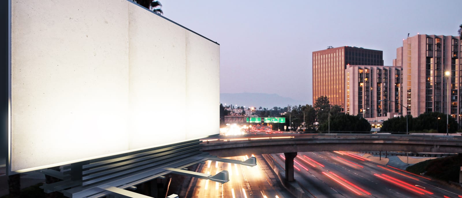 A row of illuminated billboards lining a freeway at dusk