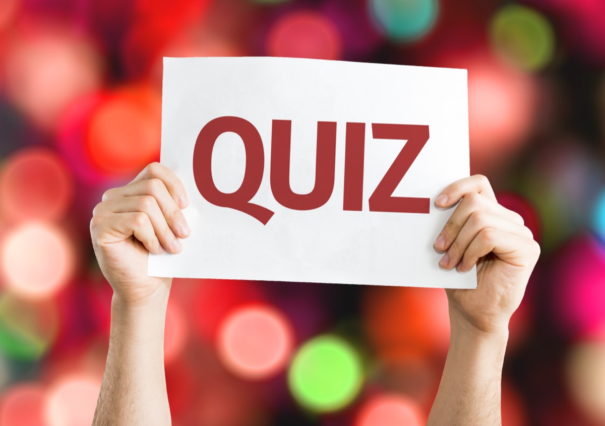 A printed trivia quiz book lying open on a table with a sharpened pencil resting across its pages