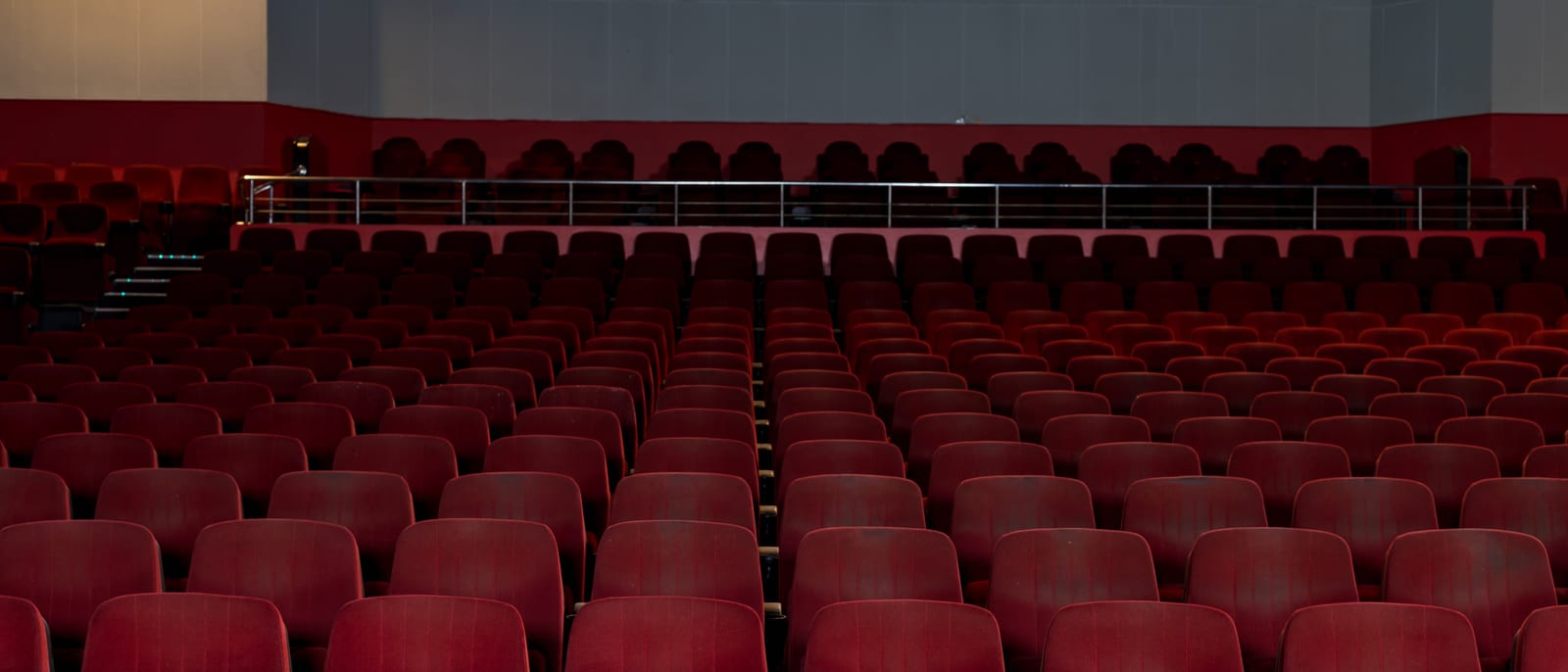An empty theater stage with a single spotlight and rows of velvet seats