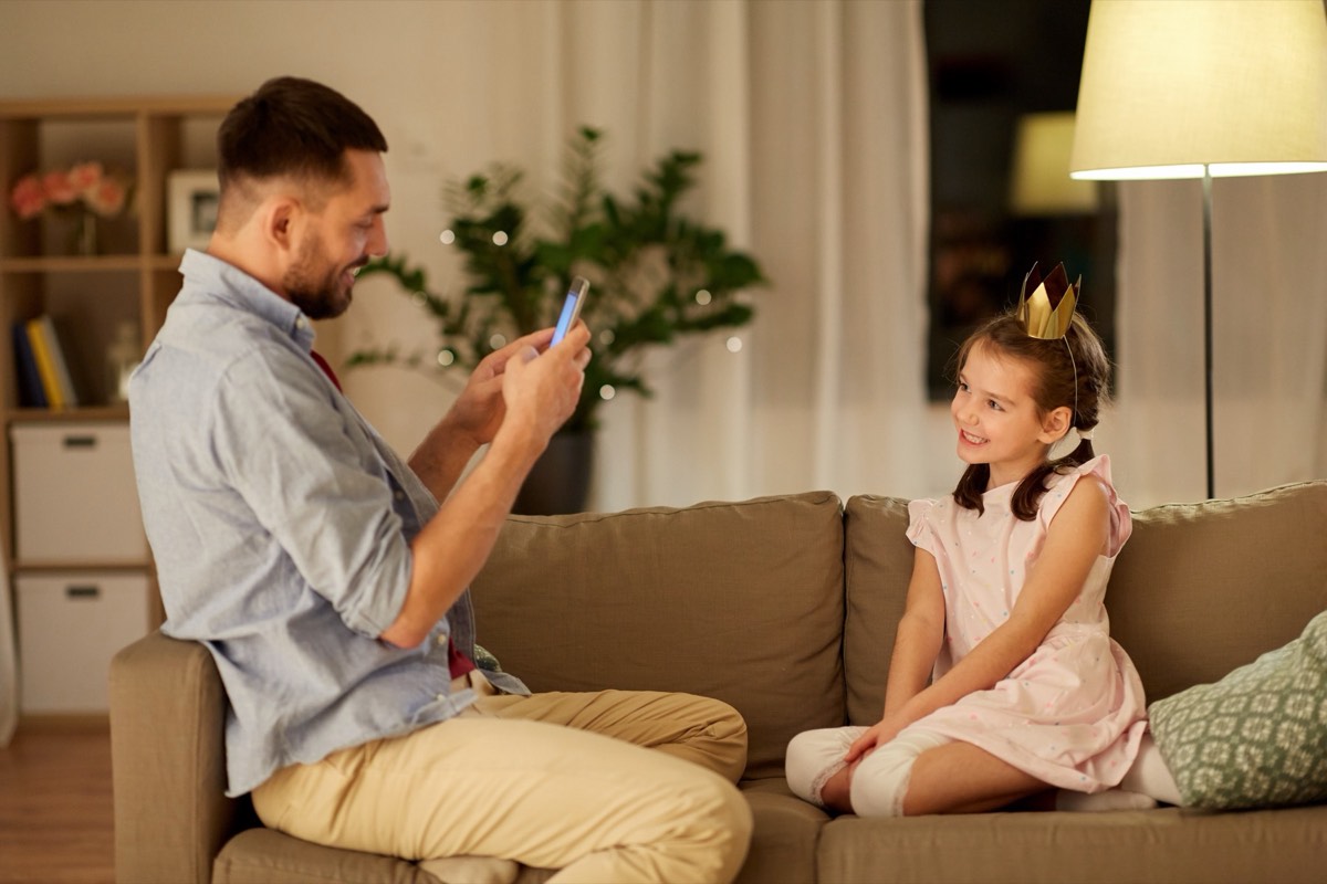 A parent recording a toddler dancing in a living room on a smartphone