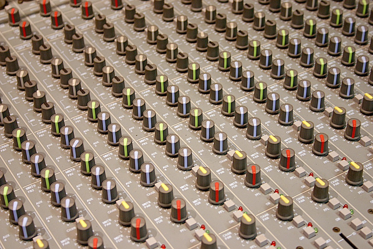 A studio mixing console with faders and meters in a dim control room