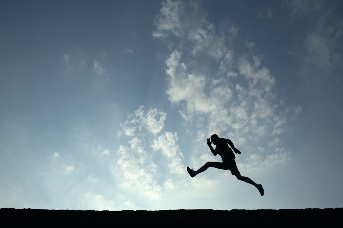 A silhouetted athlete leaping through the air against an open sky at dusk