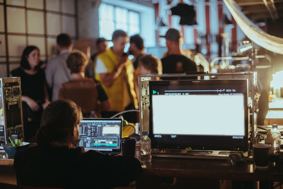 A film crew operating a cinema camera on a production set with lighting rigs in the background