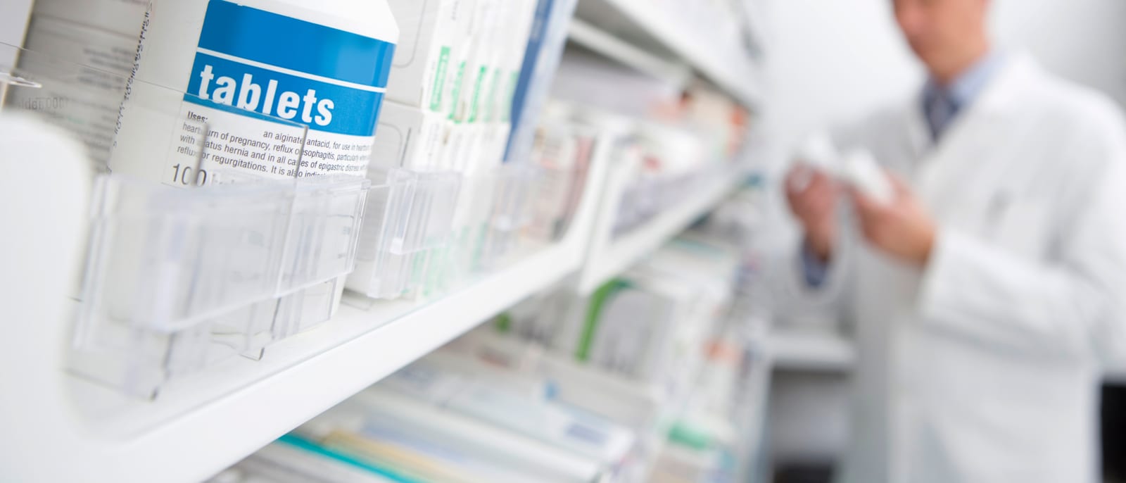 Rows of prescription pill bottles on a pharmacy shelf under bright light
