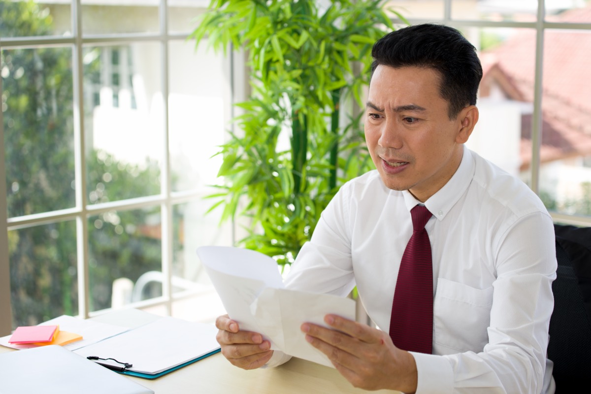 Worried small business owner reading a formal legal letter at an office desk