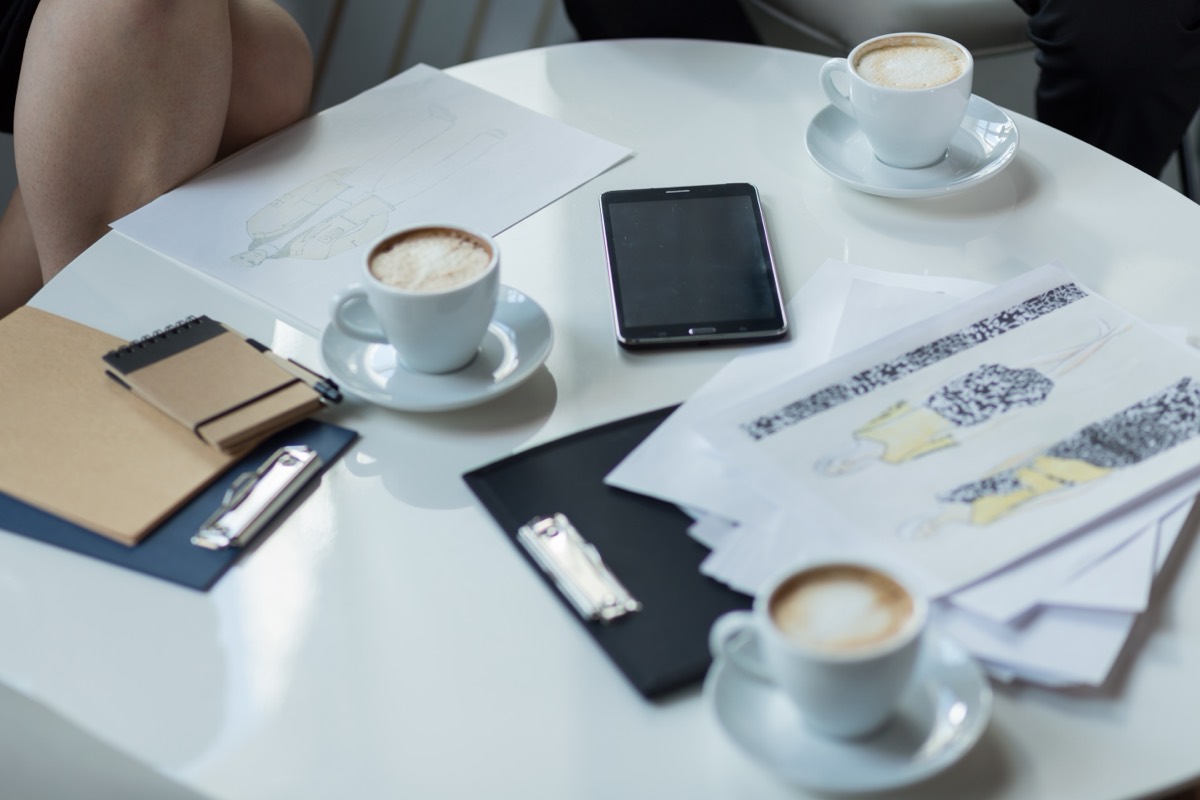 Freelance designer presenting work on a tablet to a client across a coffee shop table