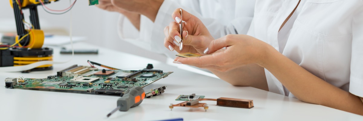 Technician repairing a game console motherboard with a screwdriver at a workbench