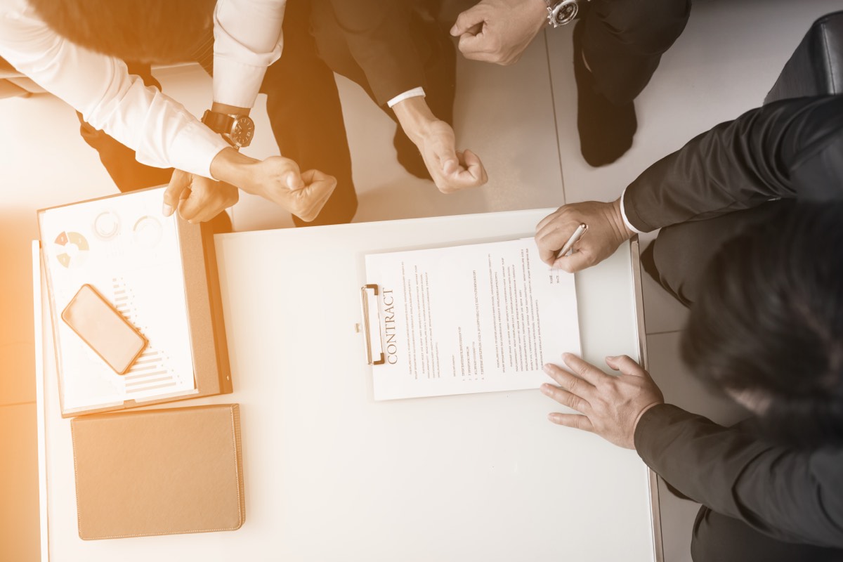 Two people signing a confidentiality agreement across a desk in a business meeting