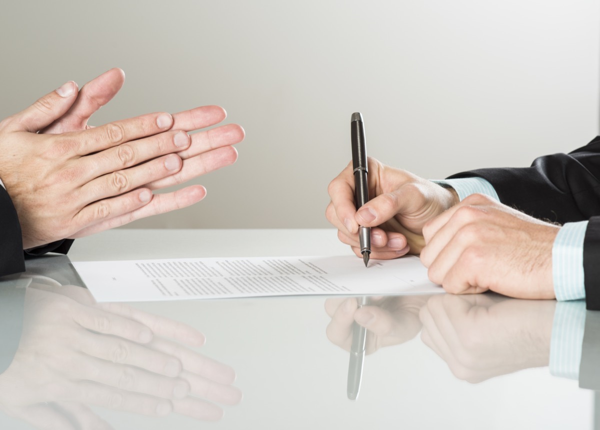 Two executives shaking hands over a signed licensing agreement