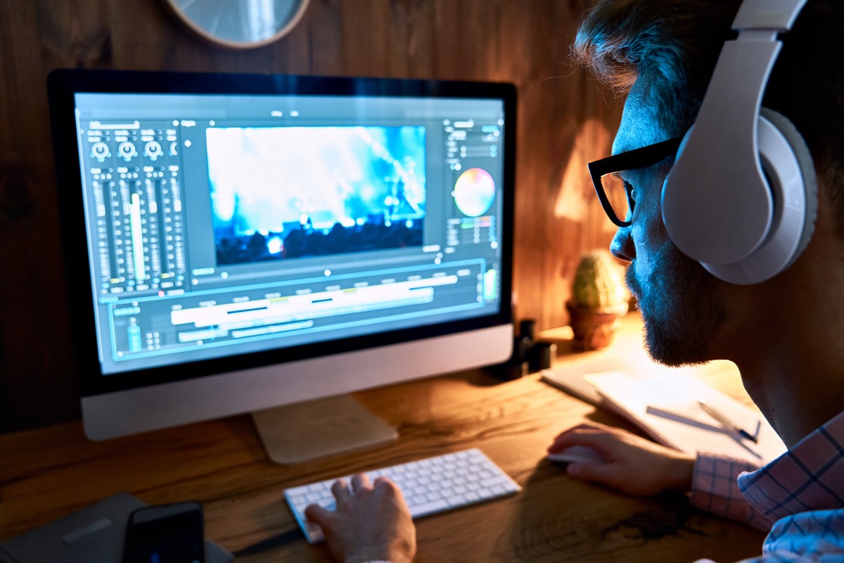 Video editor trimming film clips on a timeline across two computer monitors