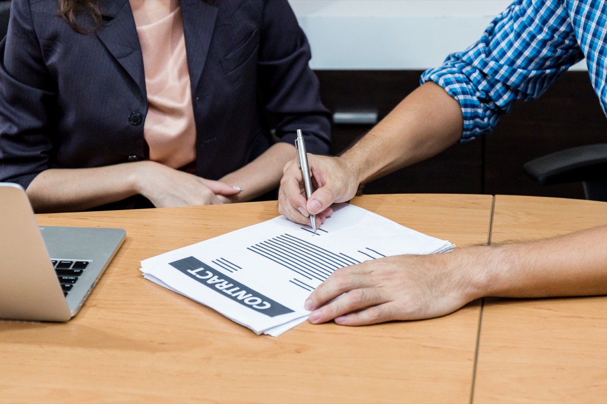 Software engineer working at an office desk with code on a monitor and a signed contract beside the keyboard