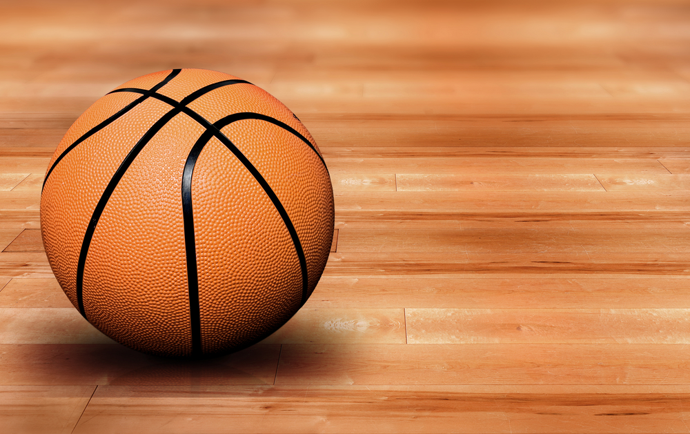 A basketball resting on a polished hardwood court under arena lighting