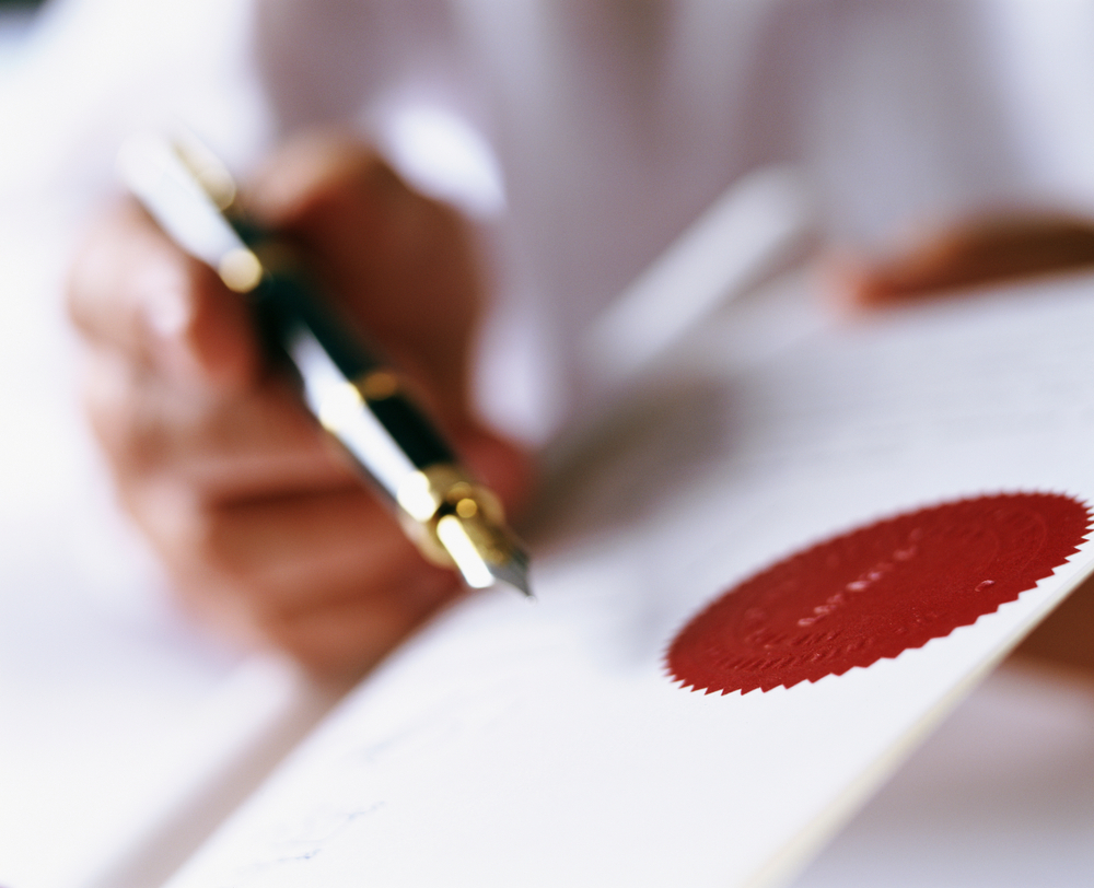 Two people signing a business licensing contract across a table with a pen