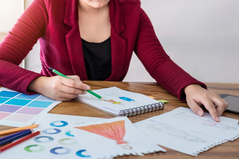 A designer's desk covered with hand-drawn fashion illustrations and colored pencils