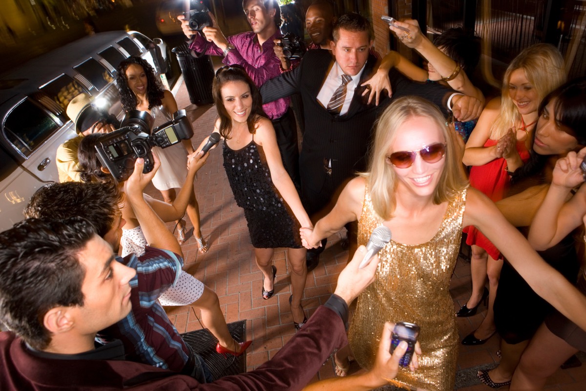 A crowd of paparazzi photographers pointing cameras with large lenses at a celebrity event