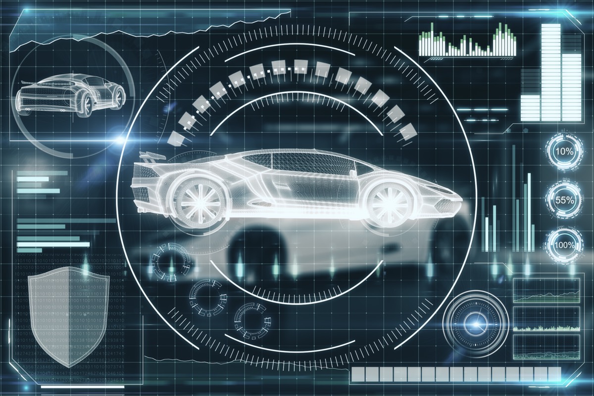 A 3D wireframe model of a car displayed on a computer monitor in a design studio
