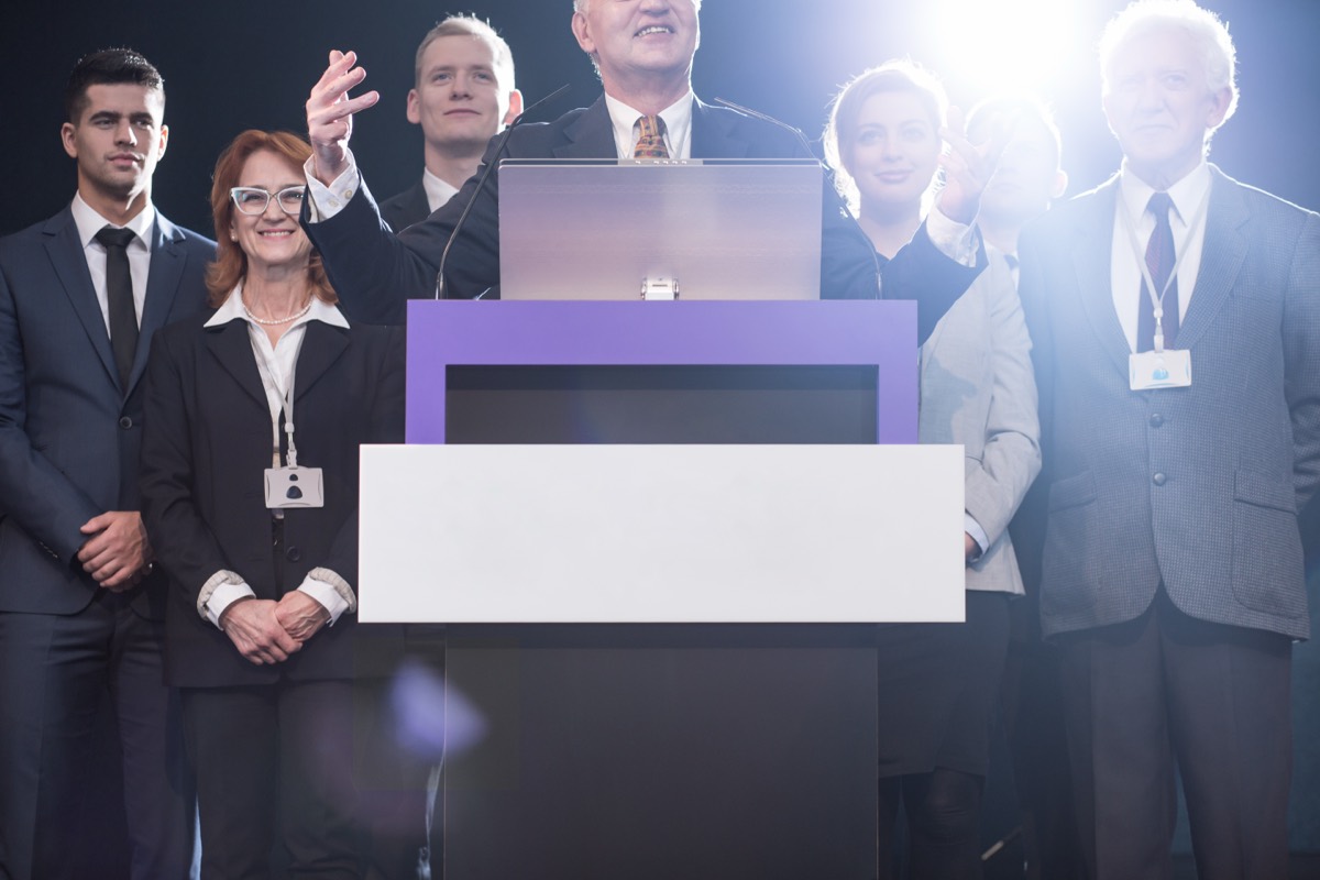 A vintage microphone on a podium before a large outdoor crowd