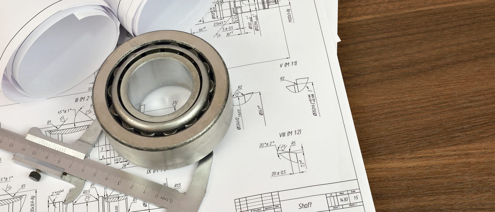 Engineering design drawings on a desk beside a metal tablet enclosure