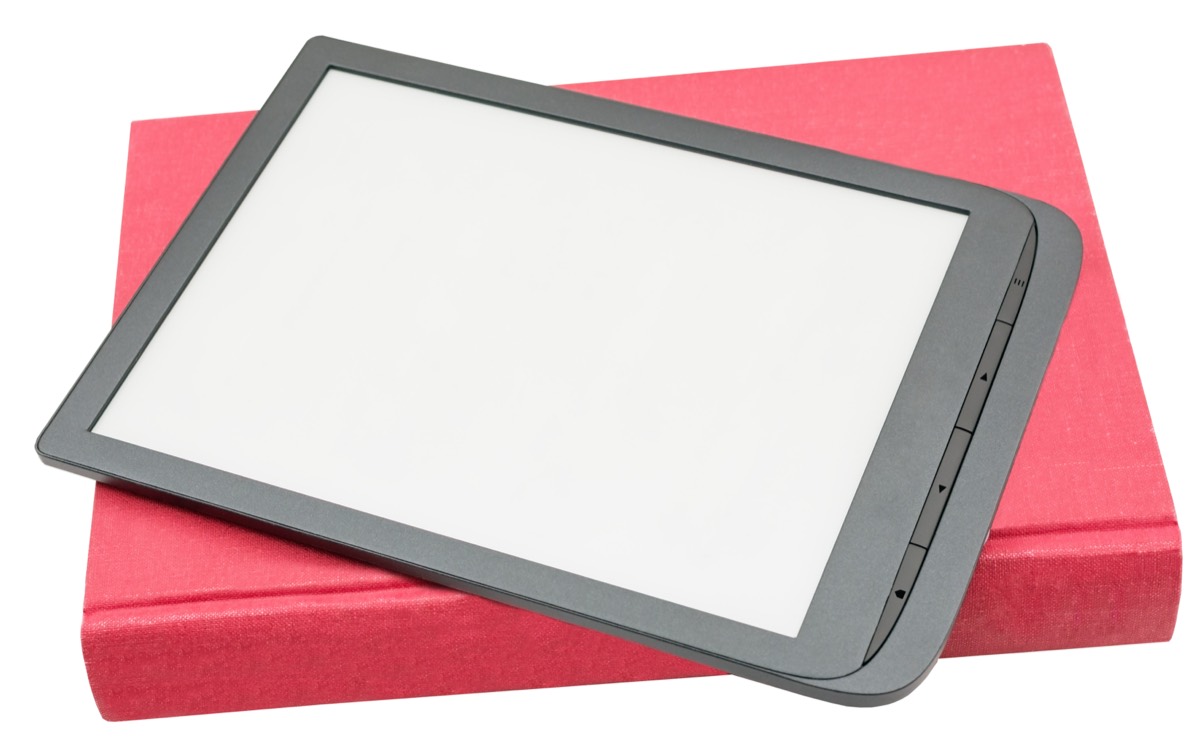 An open hardcover book lying next to an e-reader displaying digital text on a wooden table