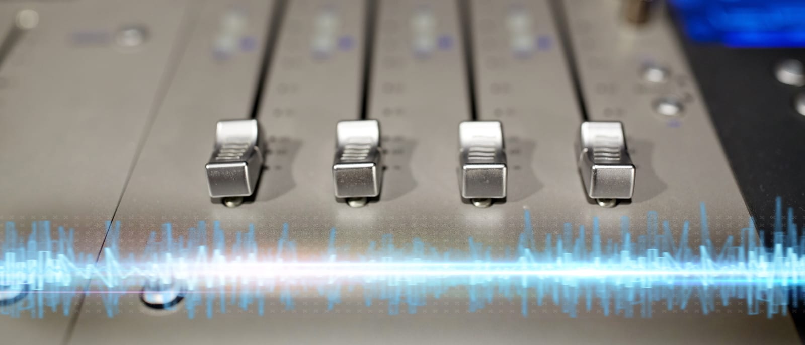 A recording studio mixing console with faders and glowing meters in low light
