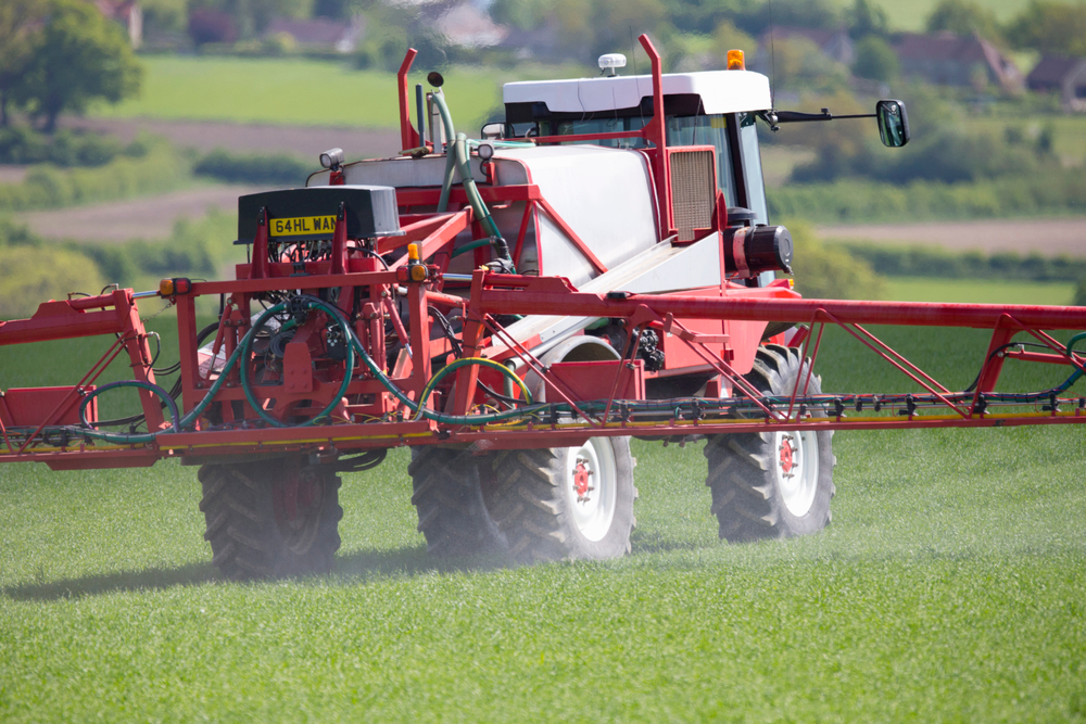 A crop-duster aircraft spraying pesticide over a green agricultural field