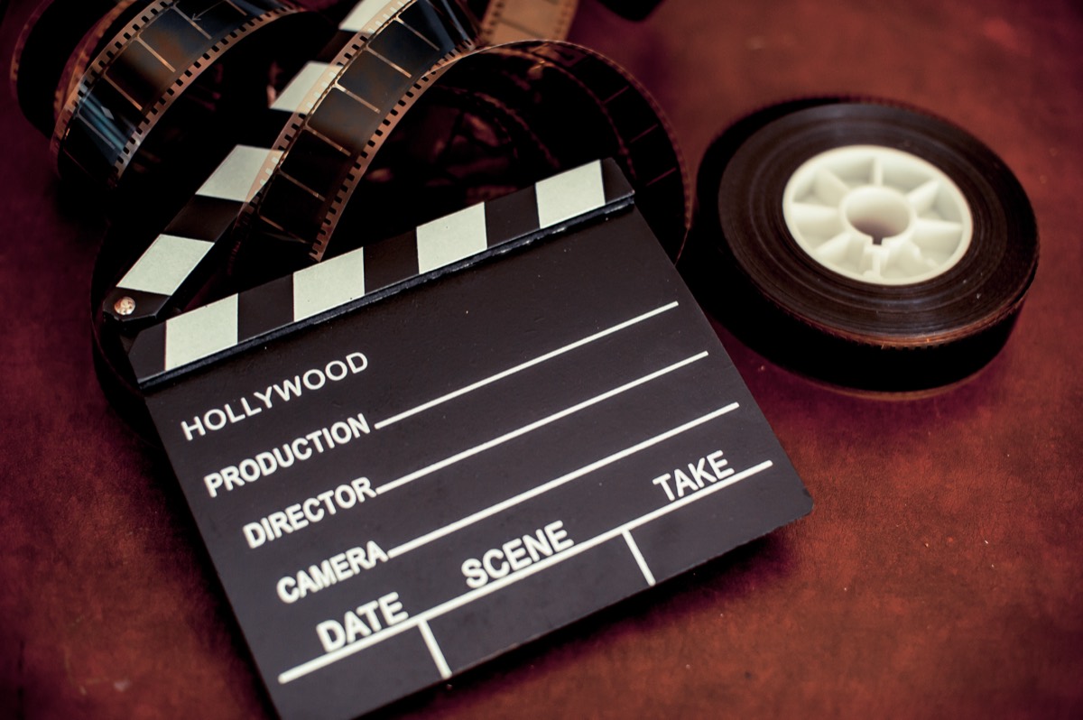A vintage film reel and clapperboard resting on a theater stage beside a script
