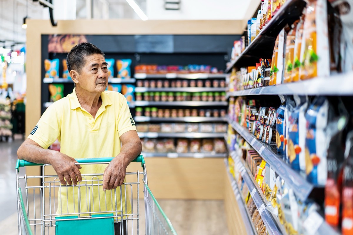 Shopper pushing a cart down a stocked supermarket grocery aisle