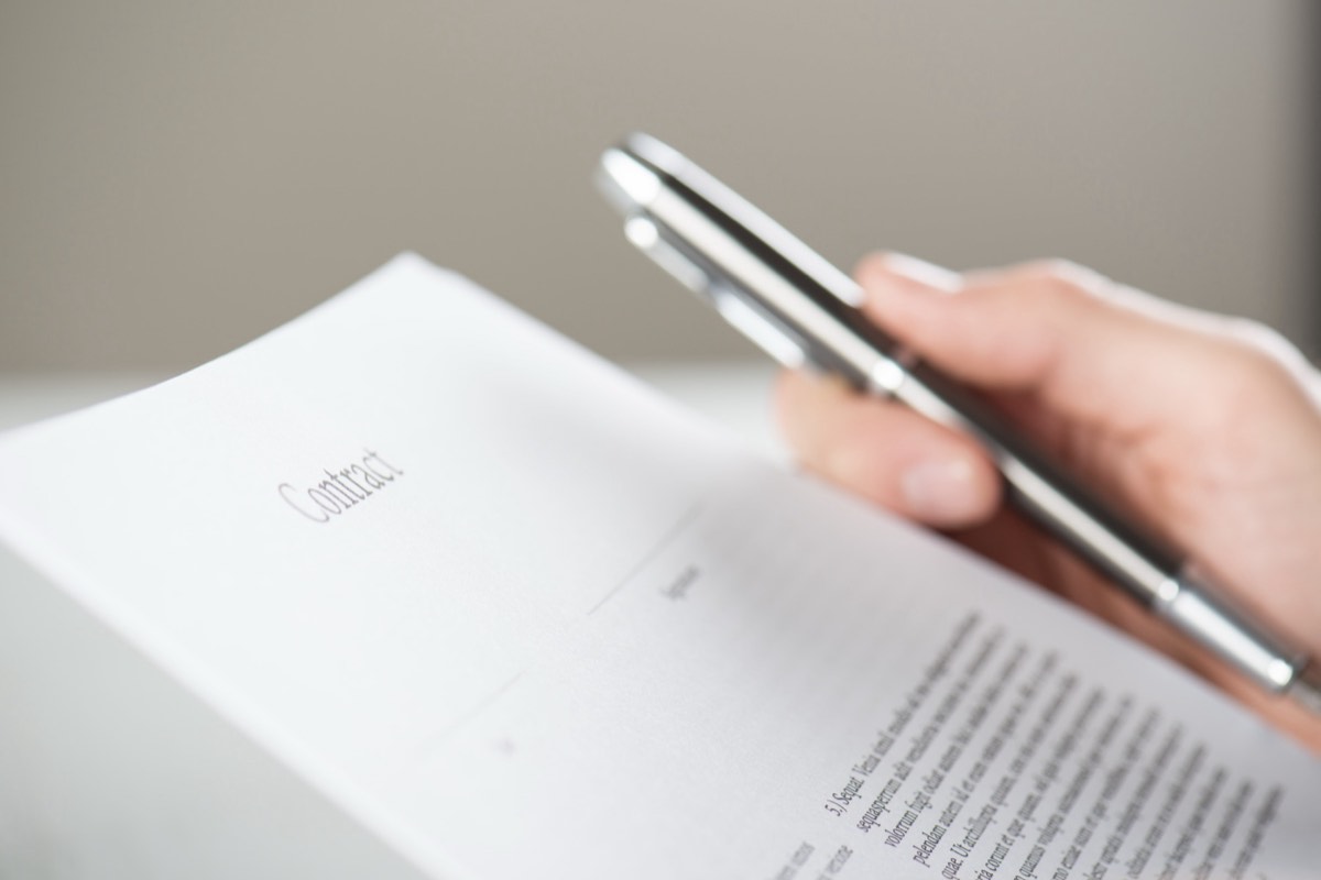 A signed contract and pen on a desk beside a stack of documents