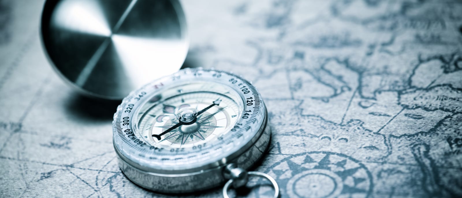 An antique world map with a brass compass resting on its surface